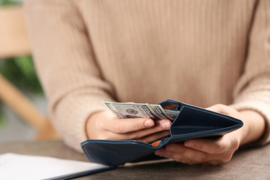 Woman putting money into wallet at brown table, closeup