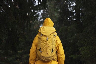 Photo of Woman with raincoat and backpack in forest under rain, back view