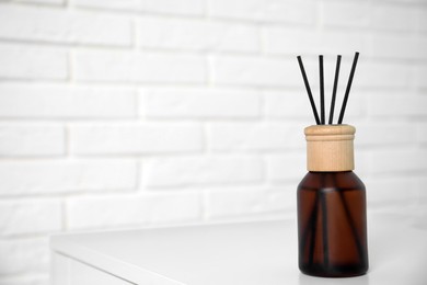 Reed diffuser on table near white brick wall. Space for text