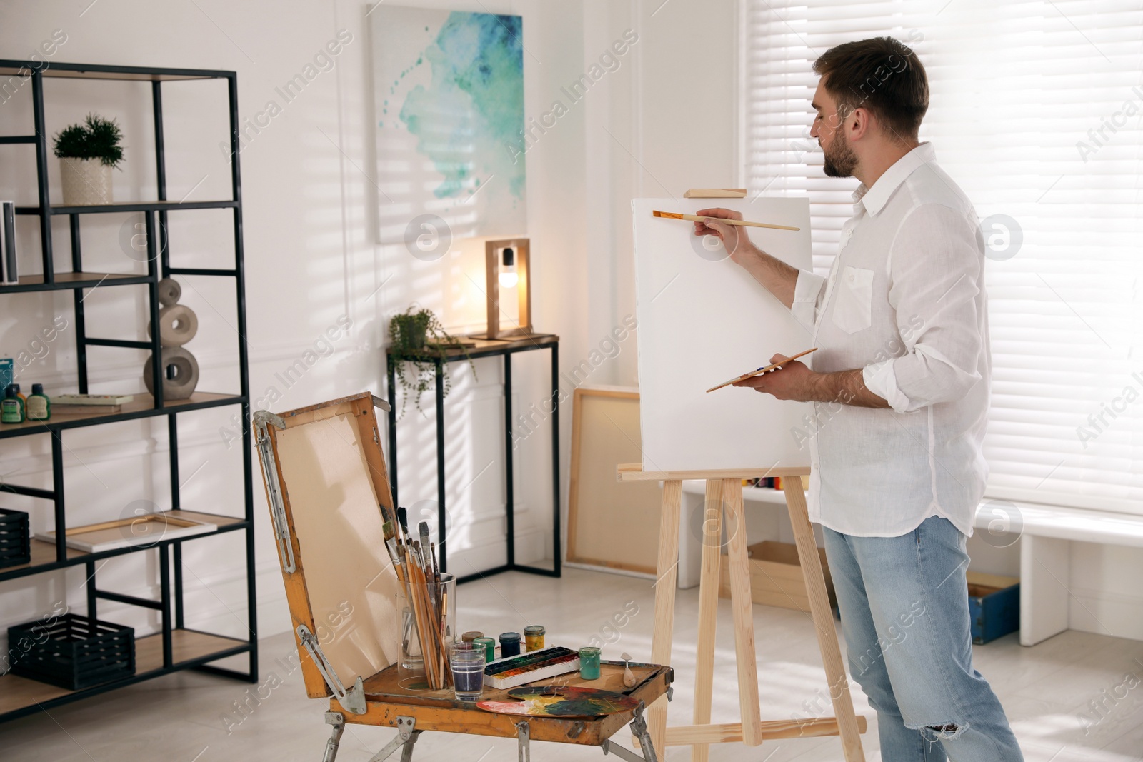 Photo of Young man painting on easel with brush in artist studio