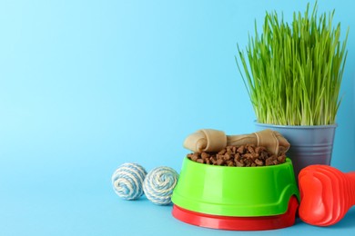 Photo of Pet toys, bowls and wheatgrass on light blue background, space for text