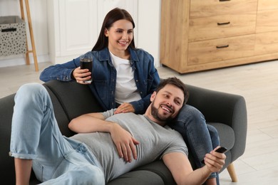 Photo of Happy couple watching show at home. Man changing TV channels with remote control