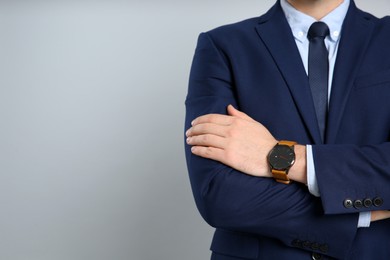 Closeup view of businessman wearing wristwatch against grey background, space for text. Time management