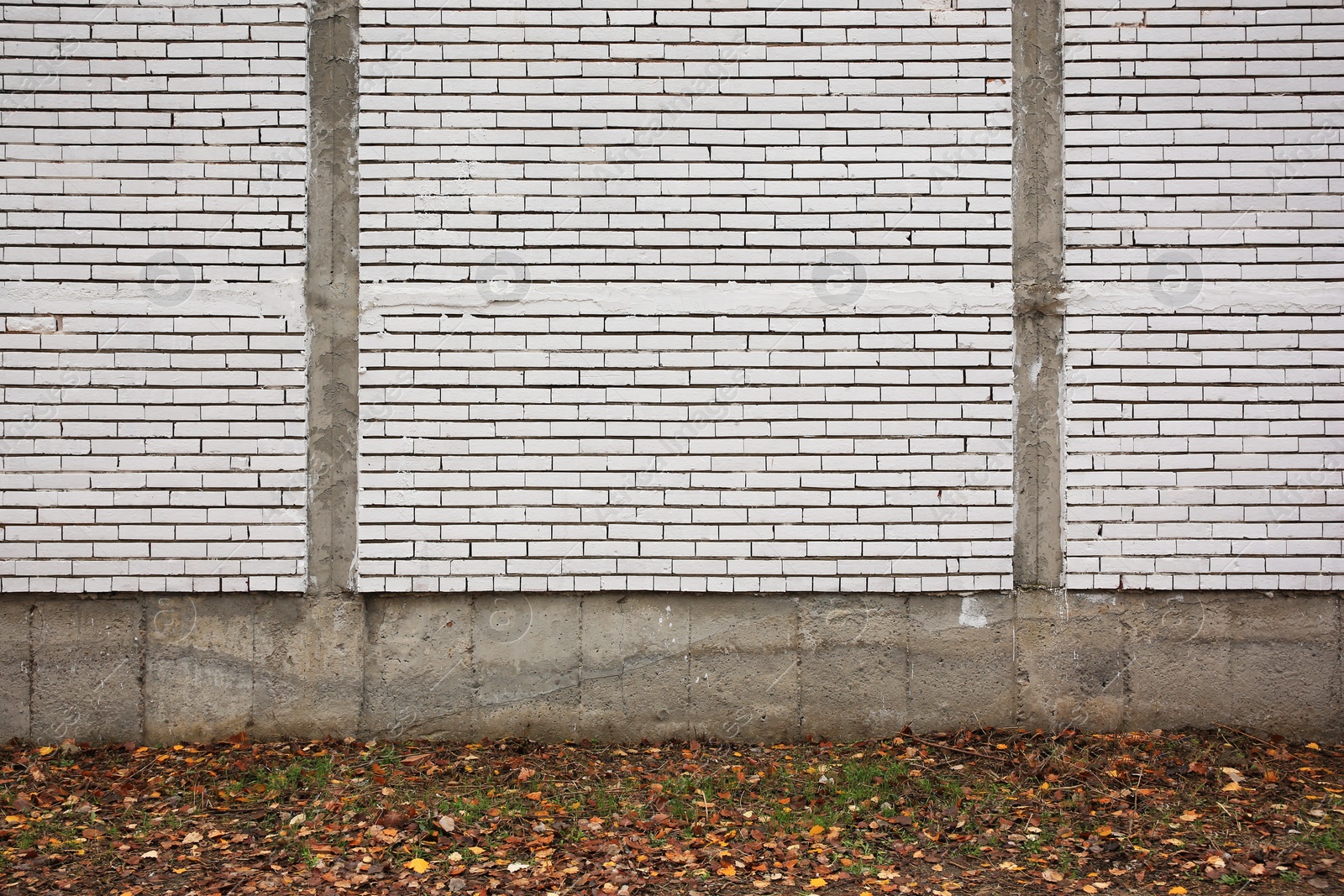 Photo of Beautiful wall made of white bricks and ground with fallen dry leaves