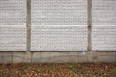 Beautiful wall made of white bricks and ground with fallen dry leaves