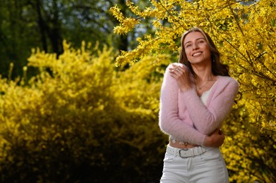 Photo of Beautiful young woman near blossoming shrub on spring day, space for text