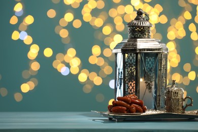 Photo of Traditional Arabic lantern, dates and vintage cup holder on table against dark turquoise background with blurred lights. Space for text