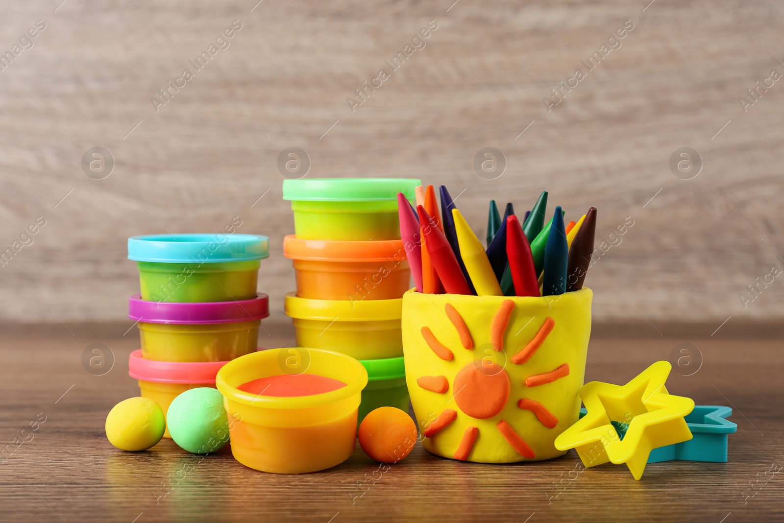 Photo of Set of bright play dough with tools and colorful pencils on wooden table