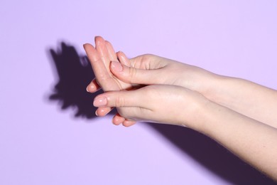 Photo of Woman applying cream on her hand against violet background, closeup