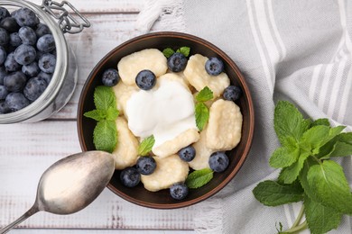Photo of Bowl of tasty lazy dumplings with blueberries, sour cream and mint leaves on white wooden table, flat lay