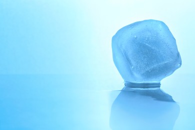 Photo of Crystal clear ice cube on light blue background, space for text. Color tone effect