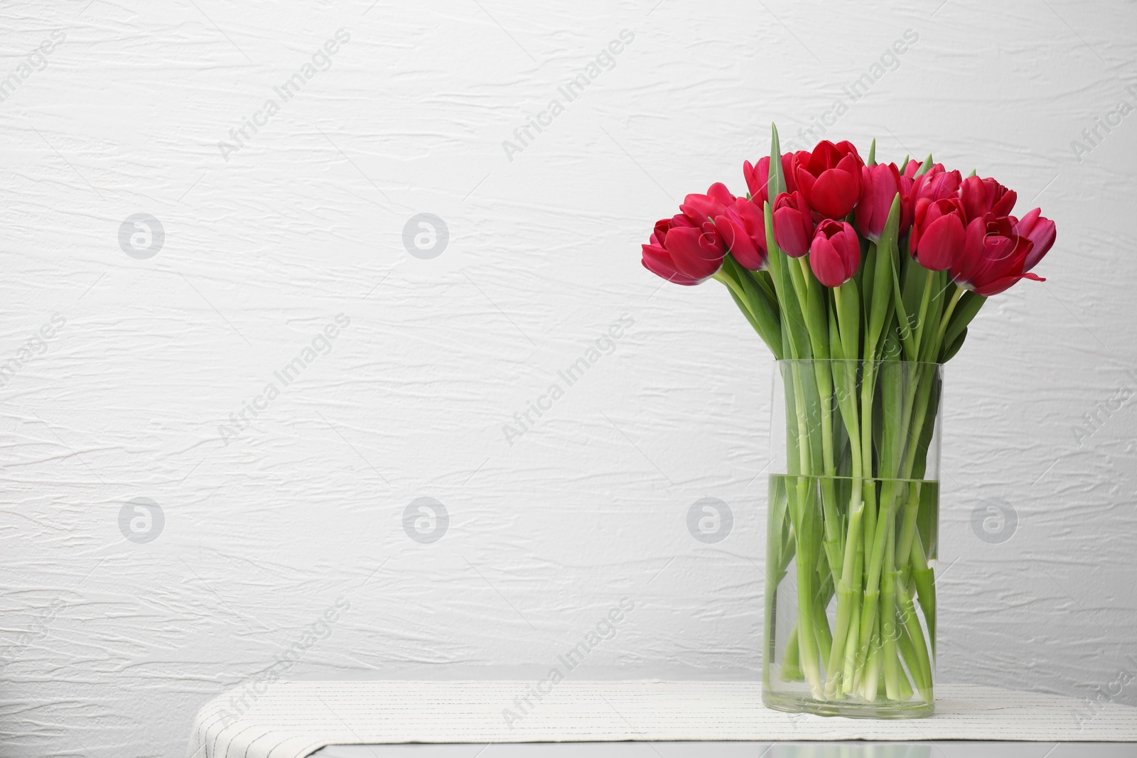 Photo of Bouquet of beautiful tulips in glass vase on table indoors. Space for text