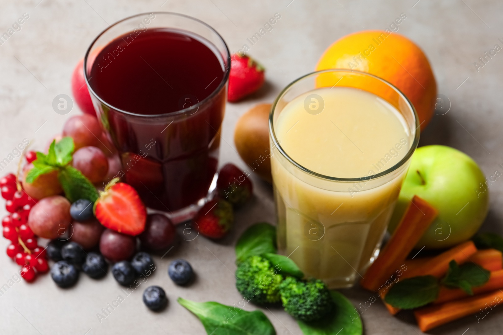 Photo of Glasses of delicious juices and fresh ingredients on grey table, closeup