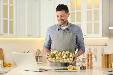 Photo of Man making dinner while watching online cooking course via laptop kitchen