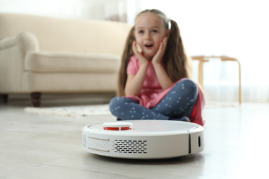 Photo of Little girl using robotic vacuum cleaner at home