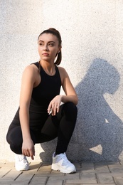 Photo of Young woman in sportswear near grey wall outdoors