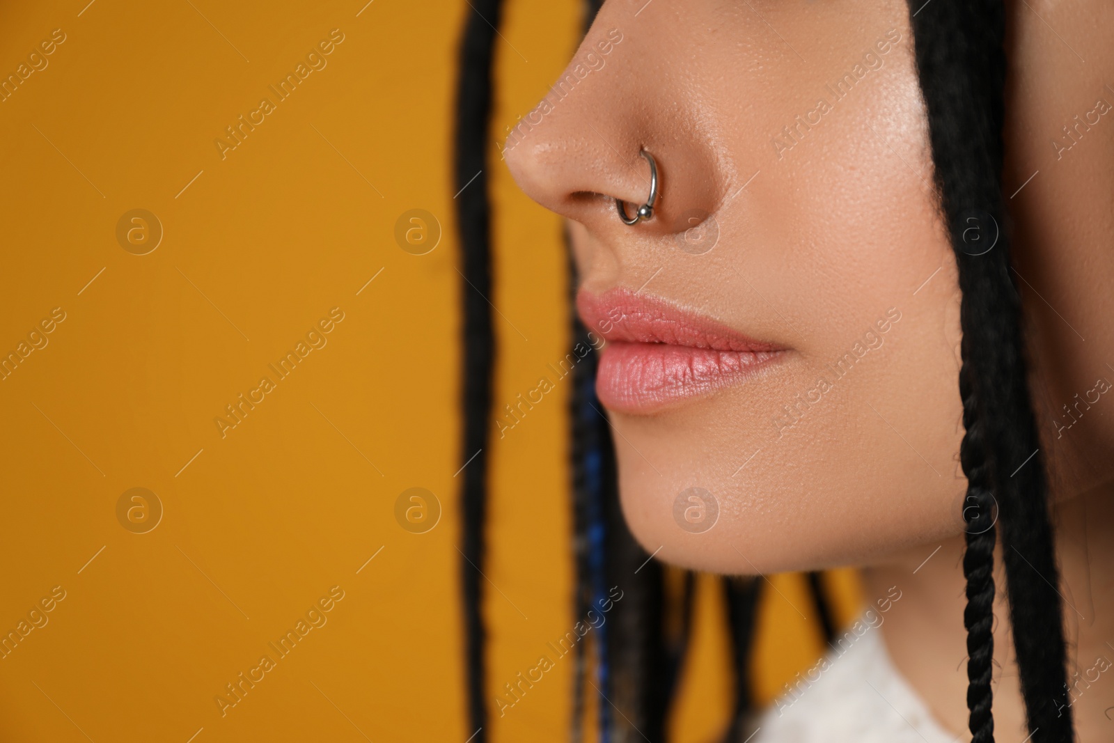Photo of Young woman with nose piercing on yellow background, closeup. Space for text