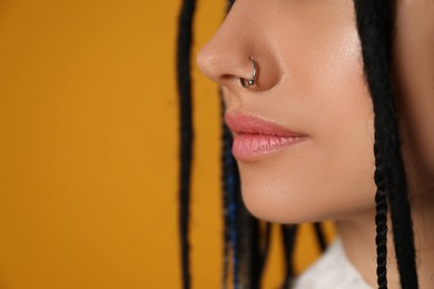 Photo of Young woman with nose piercing on yellow background, closeup. Space for text