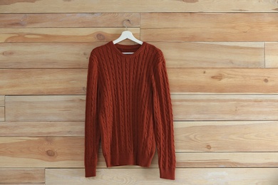 Photo of Hanger with stylish sweater on wooden wall