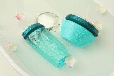 Photo of Hair care cosmetic products with flower petals and water in sink