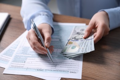 Photo of Payroll. Woman with dollar banknotes working with tax return forms at wooden table, closeup