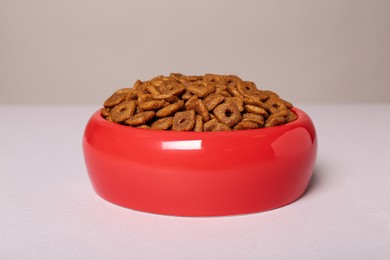 Photo of Dry food in red pet bowl on light surface