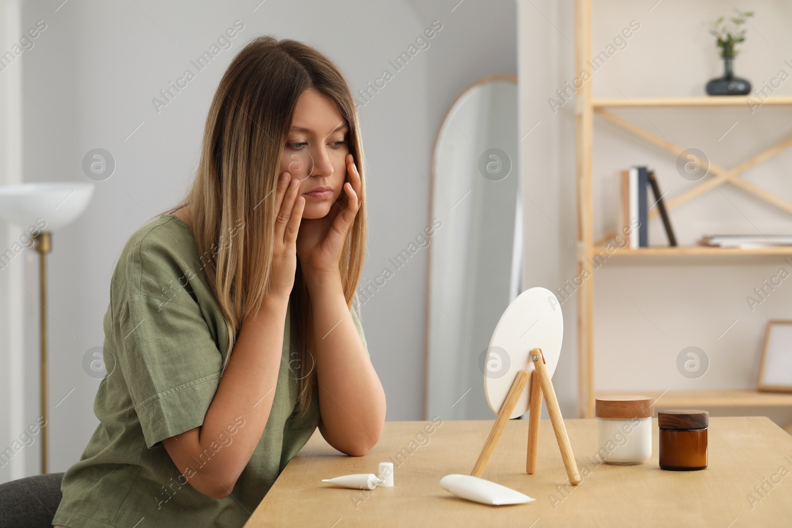 Photo of Sleep deprived young woman looking at herself in mirror indoors