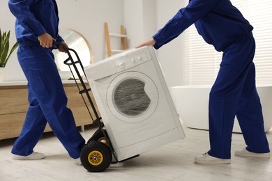 Photo of Male movers carrying washing machine in bathroom, closeup. New house