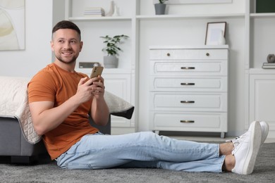 Handsome man sending message via smartphone at home. Space for text