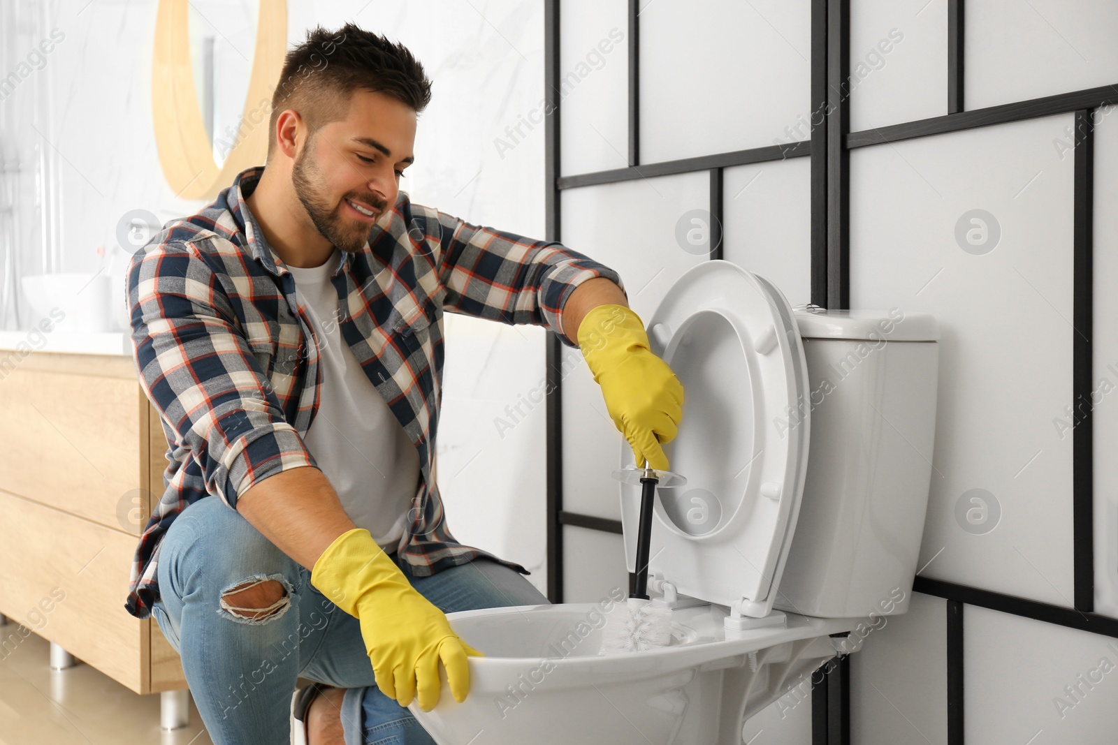 Photo of Young man cleaning toilet bowl in bathroom