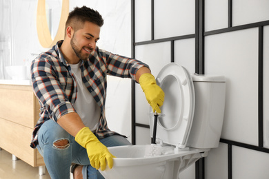 Photo of Young man cleaning toilet bowl in bathroom