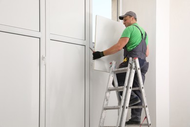 Worker on folding ladder installing window indoors