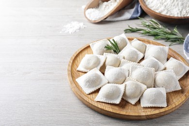 Photo of Uncooked ravioli and rosemary on white wooden table. Space for text