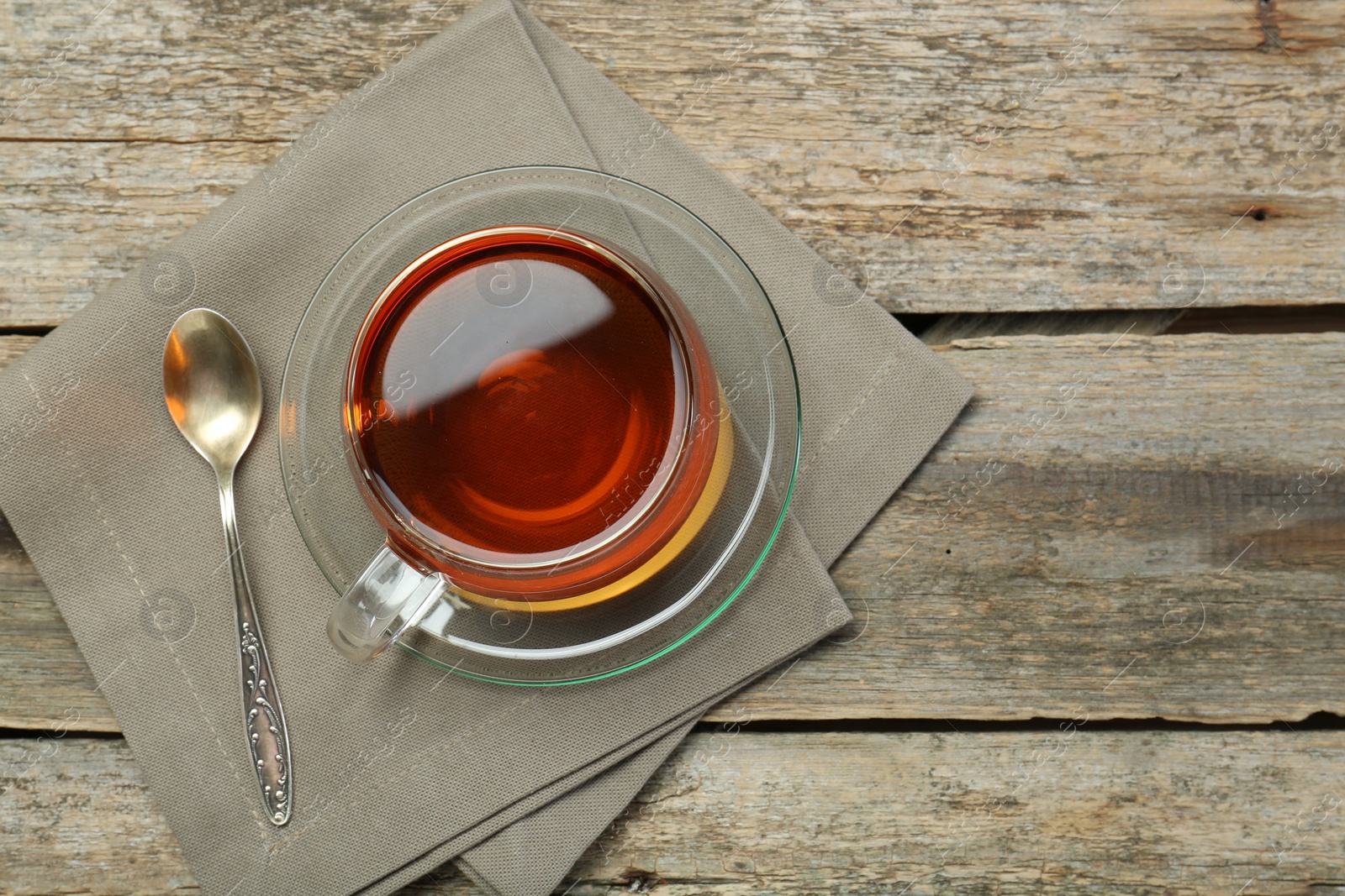 Photo of Aromatic tea in glass cup, spoon and napkin on wooden table, top view. Space for text