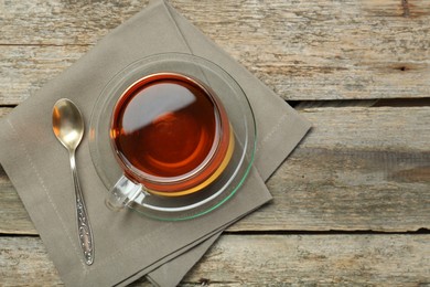 Aromatic tea in glass cup, spoon and napkin on wooden table, top view. Space for text