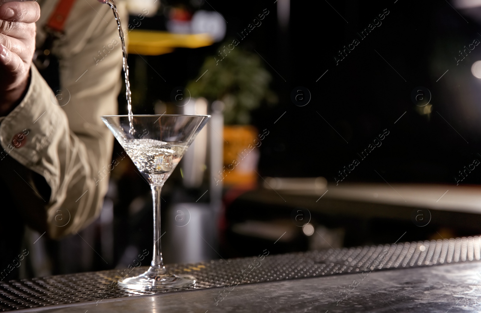 Photo of Barman pouring cold martini into glass on counter, closeup. Space for text