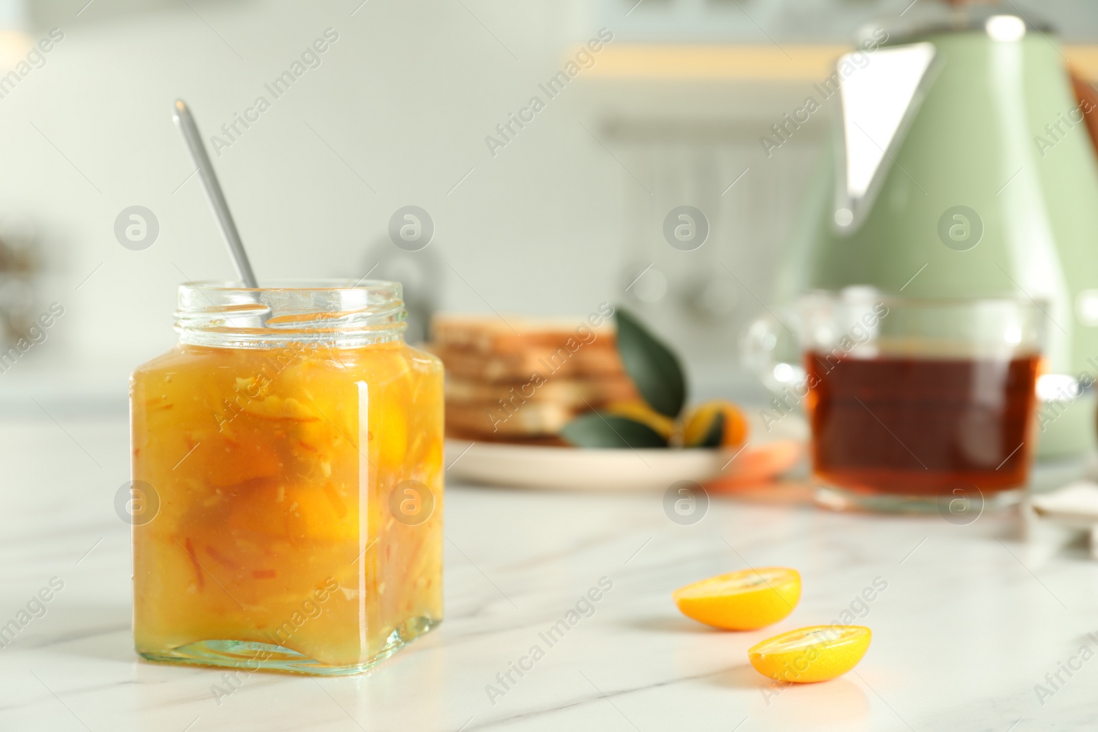 Photo of Delicious kumquat jam in jar on white marble table