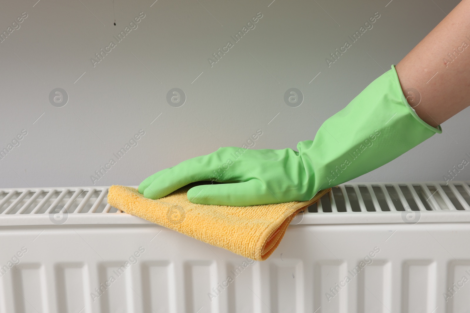 Photo of Woman cleaning radiator with rag indoors, closeup