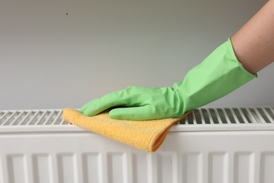 Photo of Woman cleaning radiator with rag indoors, closeup