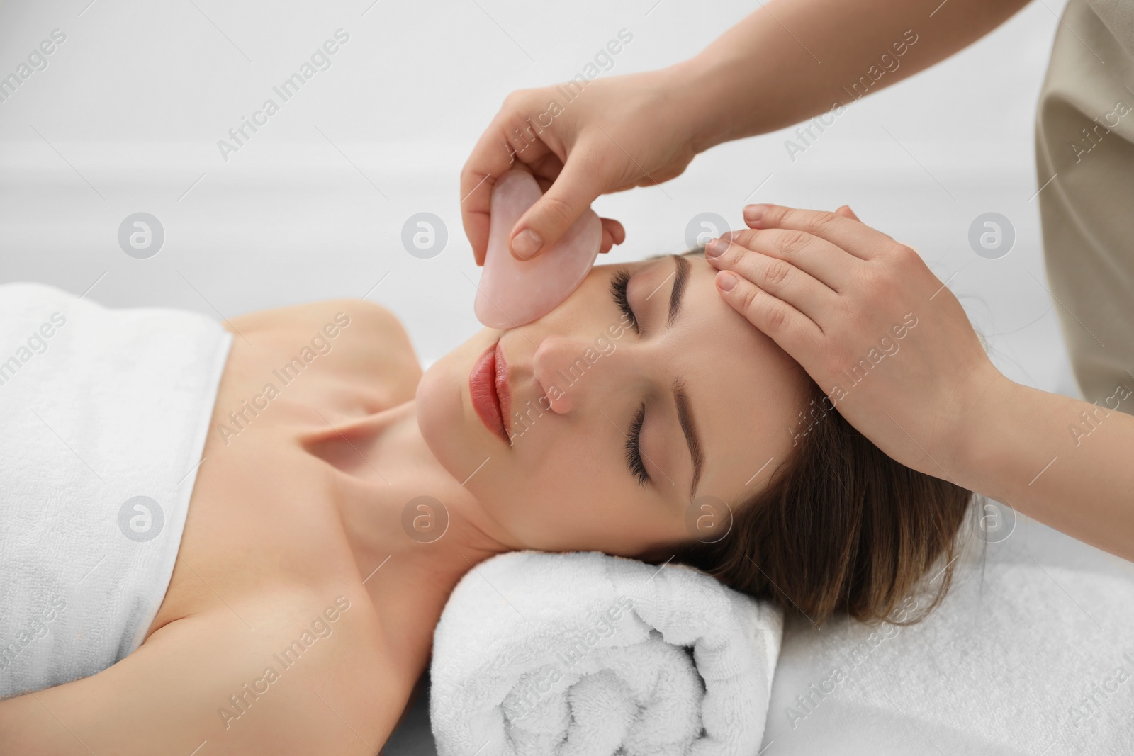 Photo of Young woman receiving facial massage with gua sha tool in beauty salon