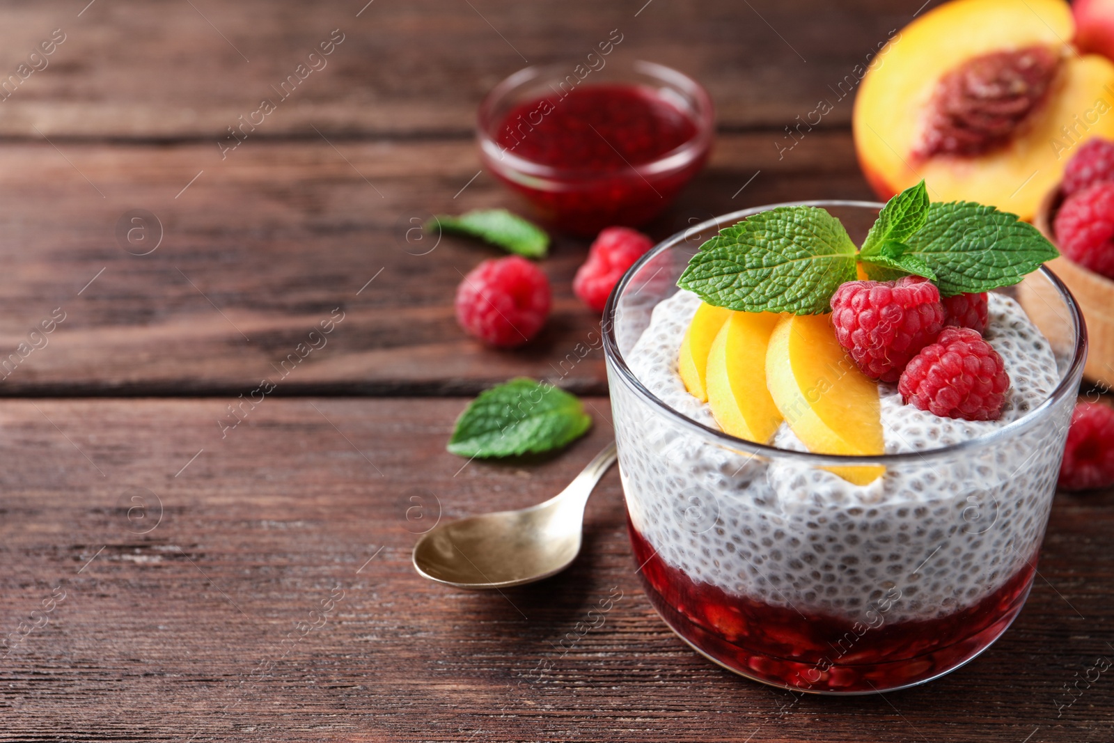 Photo of Delicious chia pudding with raspberries, peach and mint on wooden table, space for text