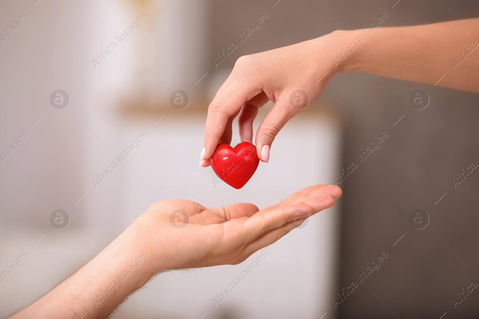 Photo of Woman giving red heart to man on blurred background, closeup. Donation concept