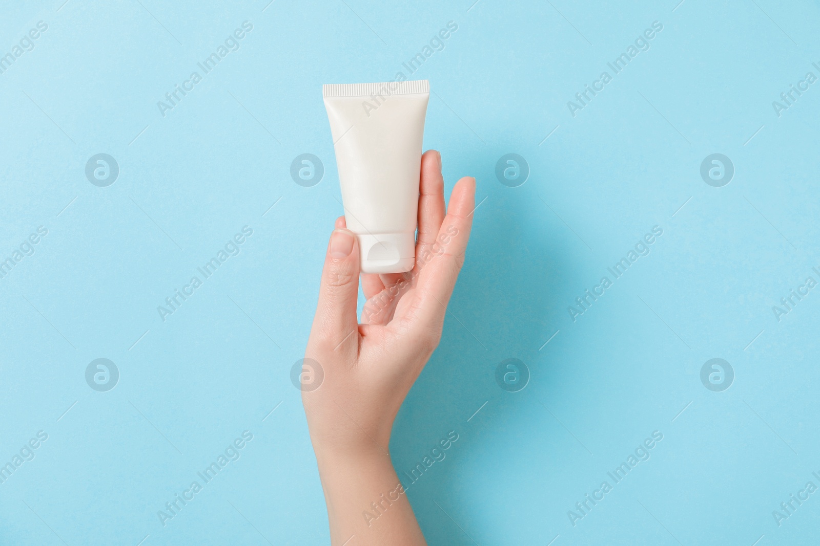 Photo of Woman with tube of hand cream on light blue background, top view