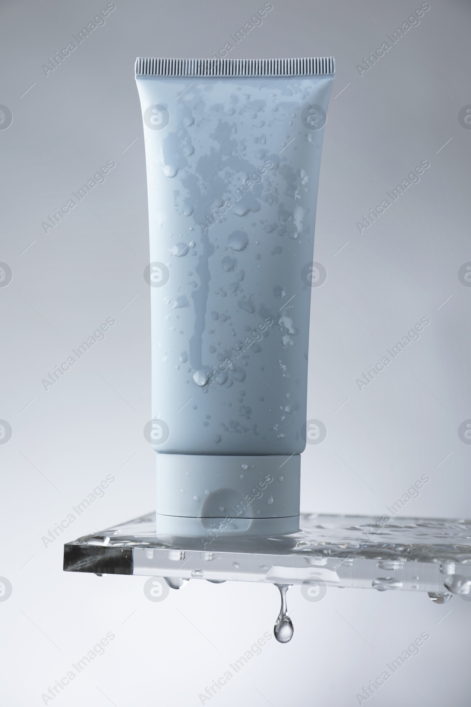 Photo of Moisturizing cream in tube on glass with water drops against grey background