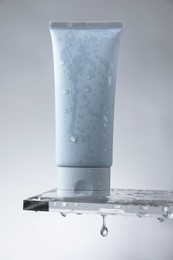 Moisturizing cream in tube on glass with water drops against grey background