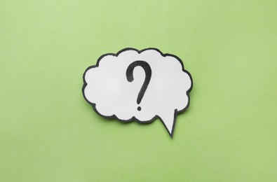 Paper speech bubble with question mark on green background, top view