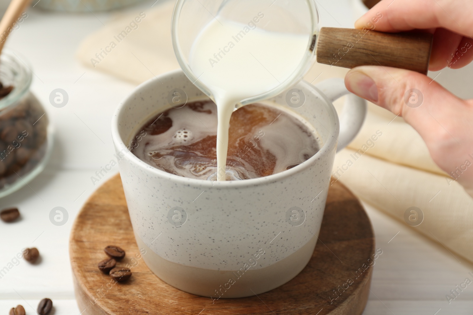 Photo of Woman pouring milk into cup with coffee at white table, closeup