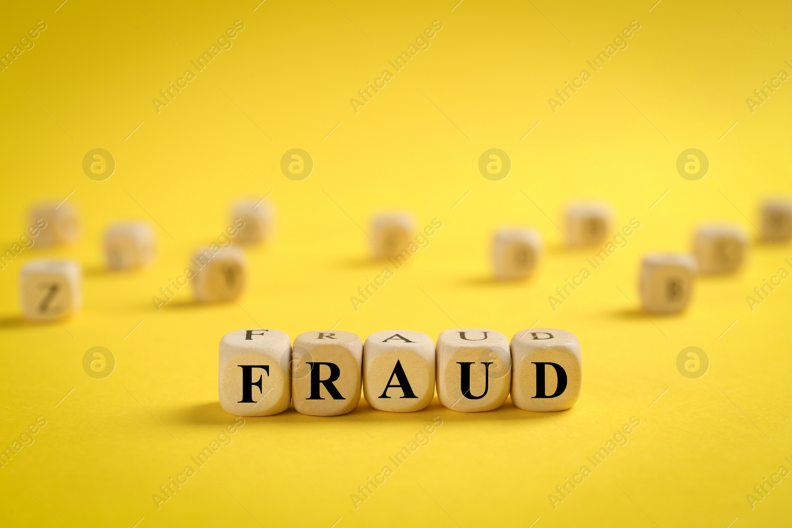 Photo of Word Fraud of wooden cubes with letters on yellow background. Space for text