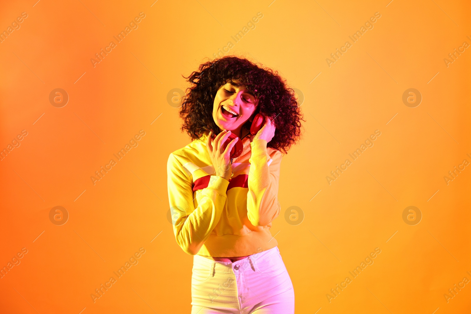 Photo of Beautiful young woman with headphones on color background in neon lights