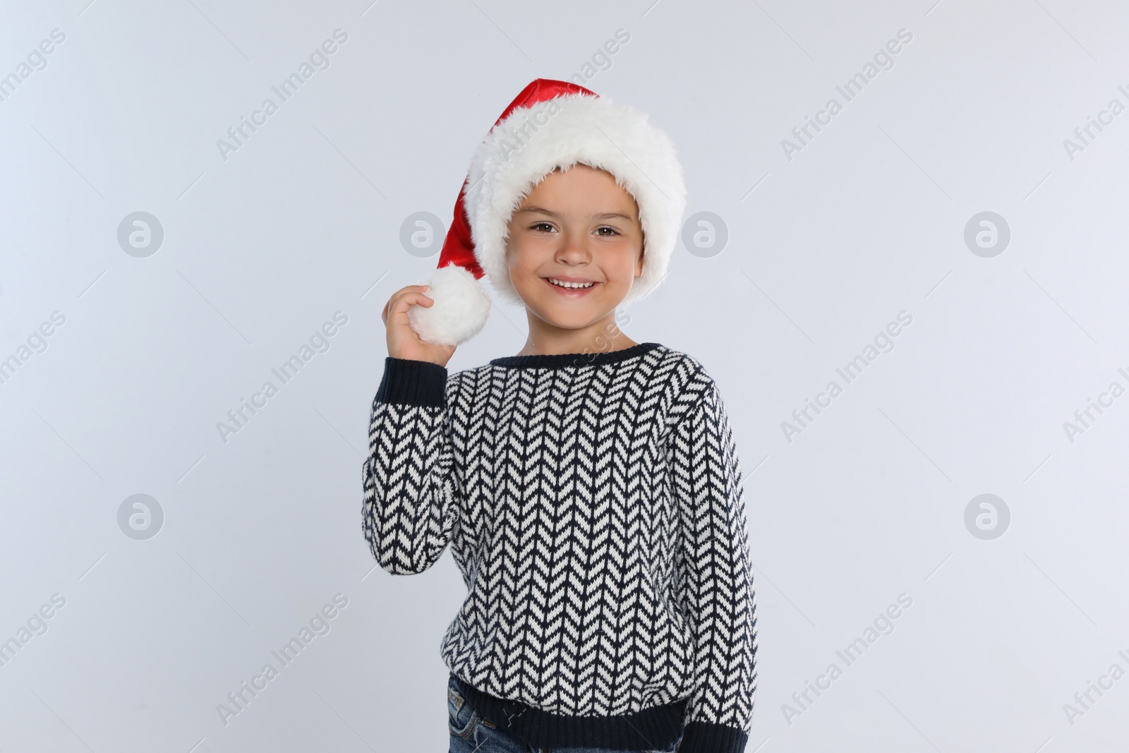 Photo of Happy little child in Santa hat on light grey background. Christmas celebration